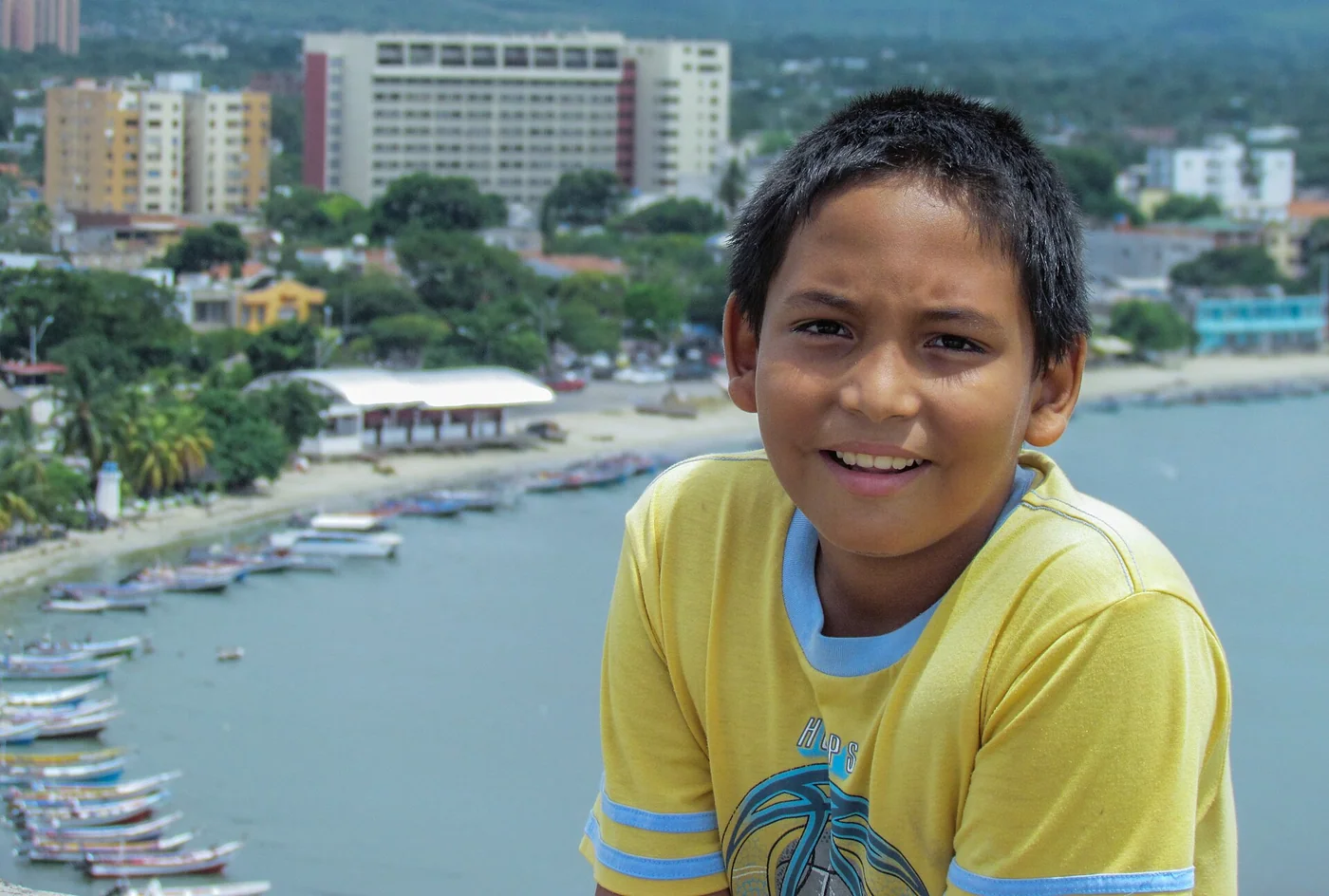 Portrait of a boy from Margarita Island, Venezuela, with the coast and town behind him.
