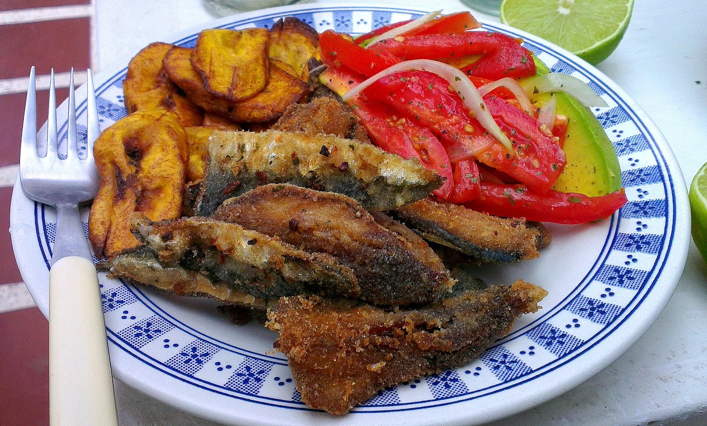 Fried sardines accompanied by tomato and avocado salad, and fried big banana